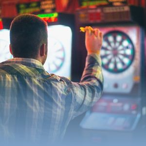 Man playing darts in a bar with electronic dart machines